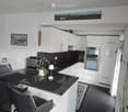 Modern kitchen with white cabinets, black countertop, and stainless steel appliances. Includes a dining area with a table and chairs.