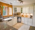 Modern kitchen with white cabinets, granite countertops, stainless steel appliances, and ample natural light from large windows.