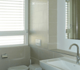 Modern bathroom with a toilet, sink, and mirror. Features tiled walls and a window with blinds.