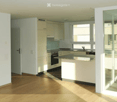 Modern kitchen with white cabinets, a central island, and a dark countertop. Features an oven, sink, and faucet, with large windows allowing natural light to fill the space.