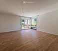 Empty room with wooden flooring, white walls, large windows, and a sliding glass door leading to a balcony.