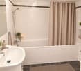 Modern bathroom with white tiles, a bathtub with a shower curtain, a sink with a modern faucet, a mirror, and decorative plants on shelves.