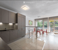 Modern kitchen with grey cabinets, a sink, and a dining area with red chairs and a glass table. Large windows and a sliding door lead to a balcony.