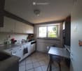 Modern kitchen with white cabinets, granite countertops, stainless steel sink, dishwasher, refrigerator, microwave, and a small dining table with a chair.