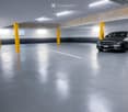 Underground parking area with a single car parked, concrete pillars, and fluorescent lighting.