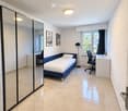 Modern, furnished bedroom with a single bed, desk, chair, mirror, and artwork on the wall.