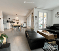 Open-plan living and dining area with a black leather sofa, wooden coffee table, dining table with chairs, and a small kitchen area with cabinets and appliances. Large sliding glass doors lead to a balcony.