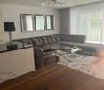 Modern living room with a grey sectional sofa, glass coffee table, wooden dining table, and decorative mirrors on the wall.