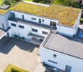 Aerial view of a modern, white house with a green roof, multiple balconies, and a swimming pool in the backyard.