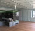 Empty room with wooden flooring, light blue walls, and a large green and black cabinet with intricate carvings. The ceiling features exposed beams and lighting fixtures.