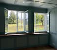 Empty room with wooden flooring, grey walls, large windows with open shutters, and a skylight ceiling.