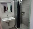 Modern bathroom with a white sink, mirror, glass shower enclosure, and a beige bathroom mat on the floor.