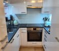 Modern kitchen with white cabinets, wooden flooring, and stainless steel appliances including an oven, induction stove, and coffee maker.