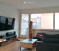 Modern living room with large windows, wooden floor, grey sofa, coffee table, TV, and speaker.