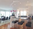 Modern open-plan kitchen and dining area with a sleek black dining table and chairs, a kitchen island with bar stools, and contemporary kitchen cabinets and appliances.