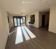 Empty room with wooden flooring, large sliding glass doors leading to a balcony, and natural light streaming in.