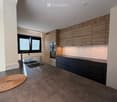 Modern kitchen with wooden cabinets, stainless steel sink, and built-in oven. Features a large window with blinds and a woven mat on the floor.