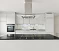 Modern kitchen with white cabinets, black granite countertop, induction cooktop, built-in oven, and stainless steel range hood.