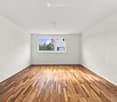 Empty room with wooden flooring and white walls, featuring a single window with a view of the outside.