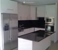 Modern kitchen with white cabinets, black countertops, stainless steel appliances including a refrigerator, microwave, and oven, and a central island.