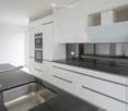 Modern kitchen with white cabinets, black countertops, stainless steel sink, and built-in oven.