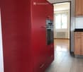 Modern kitchen with red cabinetry, stainless steel oven, and wooden flooring.