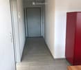 A clean, modern hallway with tiled flooring, white walls, and a wooden table on the right side. A closed door is visible at the end of the corridor.