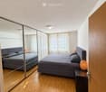 Modern bedroom with a large bed, nightstand, lamp, and a large mirror reflecting the room.