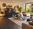 Modern living room with dark wooden flooring, large windows, and contemporary furniture including a sofa, chairs, a coffee table, and a bookshelf.