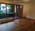 Empty room with wooden flooring, large sliding glass doors leading to a balcony, radiator, and visible outdoor view.