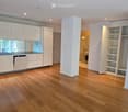 Open-plan unfurnished room with light wooden flooring, white cabinetry, and built-in shelving. The space includes a kitchen area with integrated appliances and a separate storage area with open shelves.