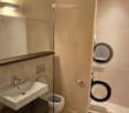 Modern bathroom with a white sink, toilet, and a glass-enclosed shower area. A washing machine is visible in the background.