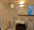 Modern bathroom with beige tiles, a glass-enclosed shower, a floating sink with a dark wooden cabinet, and a toilet.