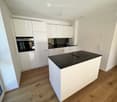 Modern kitchen with white cabinets, black countertop, built-in oven, sink, and faucet.