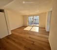 Empty room with wooden flooring, white walls, and a large sliding glass door leading to a balcony area.