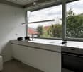 Modern kitchen with white cabinets, stainless steel appliances, and large windows overlooking a garden.