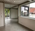 Empty room with concrete floor, large windows, and sliding glass doors leading to a balcony.