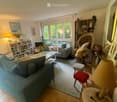 Bright living room with large windows, two sofas, coffee table, bookshelf, wicker chair, and decorative items.