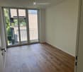Empty room with light wooden flooring, white walls, and large sliding glass doors leading to a balcony.