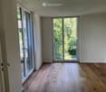 Empty room with wooden flooring, large windows, and sliding glass doors leading to a balcony.