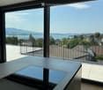 Modern room with large windows offering a scenic view of a lake and mountains, featuring a sleek wooden table with a laptop on it.