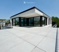 Modern rooftop terrace with large glass sliding doors, white tiled floor, and metal railings.