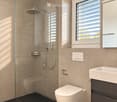 Modern bathroom with beige tiles, black marble flooring, a glass-enclosed shower, a toilet, a sink with a dark cabinet, and a window with blinds.