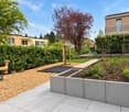 Well-maintained garden with a wooden seesaw, climbing frame, raised garden beds, and neatly trimmed hedges.