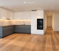 Modern kitchen with white cabinets, dark lower units, wooden flooring, and built-in appliances including a sink and oven.
