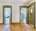 Empty hallway with wooden herringbone flooring, white walls, and green double doors leading to other rooms.
