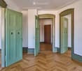Empty hallway with wooden herringbone flooring, light-colored walls, and several green doors leading to other rooms.