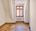 Empty room with wooden herringbone flooring, white walls, and a large window with wooden frame. A radiator is mounted below the window.