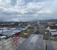 Shared rooftop terrace with a cityscape view, featuring a table and chairs, a wooden bench, and a metal railing.
