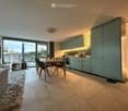 Open-plan living and dining area with a modern kitchen, dining table, chairs, sofa, and a large window with a view.